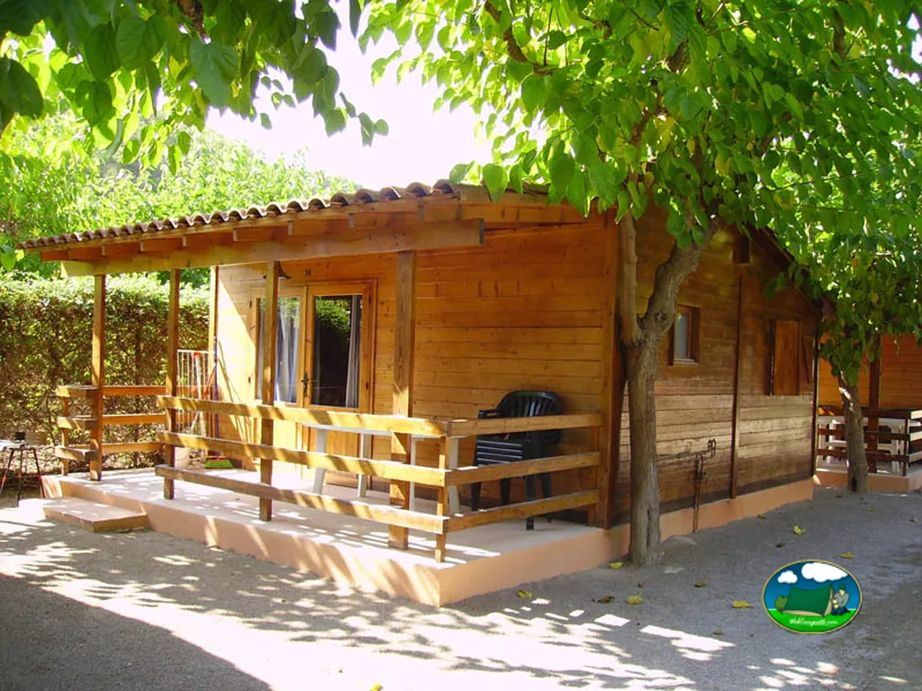 Cabaña de madera con porche y sombra de árboles del Camping Trillas Platja Tamarit, Tamarit (Tarragona)