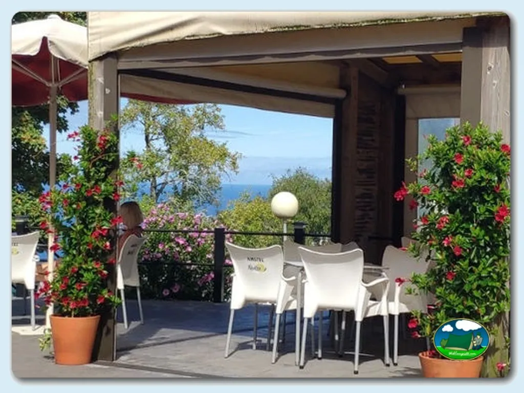 Restaurante con vistas al mar, flores rojas y sombrilla del Camping Santa Elena, Mutriku (Gipuzkoa)