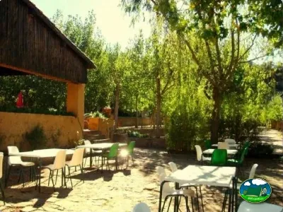 Área de descanso con mesas y sillas bajo árboles del Camping El Puente, Rodellar (Huesca)