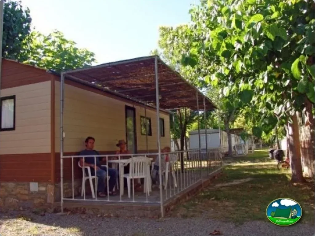 Mobil-home con terraza y sombrilla entre árboles del Camping Peña Montañesa, Labuerda (Huesca)