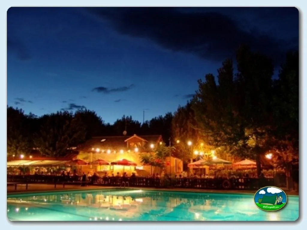 Piscina iluminada al atardecer con restaurante y bungalows del Camping Peña Montañesa, Labuerda (Huesca)