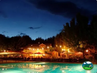 Piscina iluminada al atardecer con restaurante y bungalows del Camping Peña Montañesa, Labuerda (Huesca)