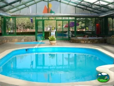 Piscina climatizada cubierta con vistas al parque infantil del Camping Peña Montañesa, Labuerda (Huesca)