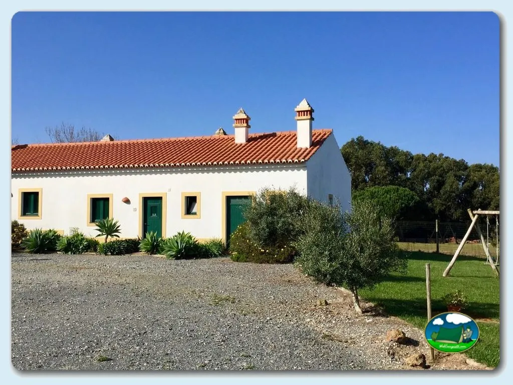 Cabaña blanca con tejado de barro y parque infantil del Camping Monte Carvalhal da Rocha, Odemira (Beja)