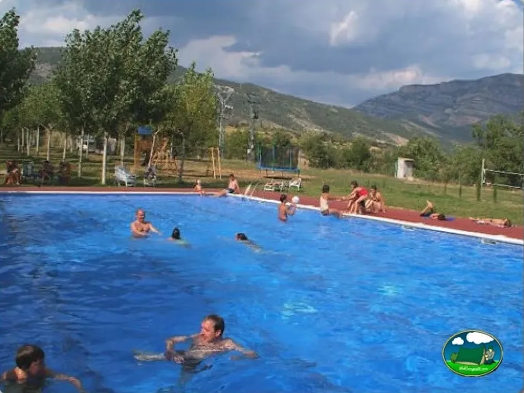 Piscina con vistas a la montaña, gente bañándose y parque infantil del Camping Isabena, La Puebla de Roda (Huesca)