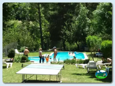 Piscina con zona de césped, sombrillas y zona de juegos infantiles del Camping Can Roig, Cóll (Lleida)