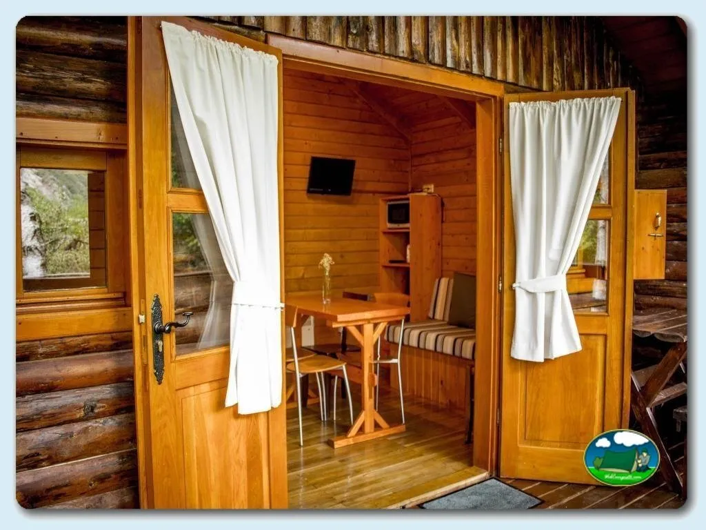 Cabaña de madera con interior amueblado y cortinas blancas del Camping Bedura Park, Val D'Aran (Lleida)