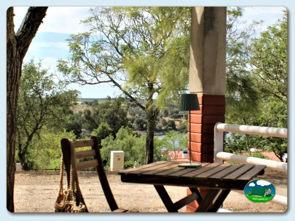 Parcela con vistas al río y sierra, zona de estar bajo árboles del Camping Albufeira do Maranhão, Avis (Portalegre)