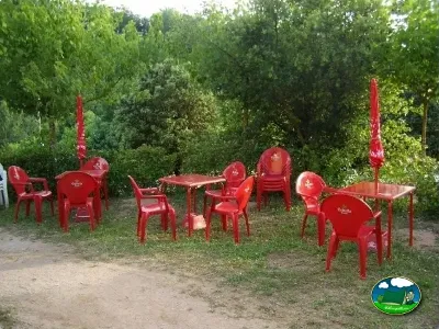 Zona de estar con mesas y sillas rojas entre árboles del Camping La Balma, Espinelves (Girona)