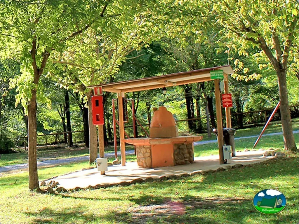 Parque infantil con barbacoa entre árboles del Camping Masia Sadernes, Sadernes (Girona)