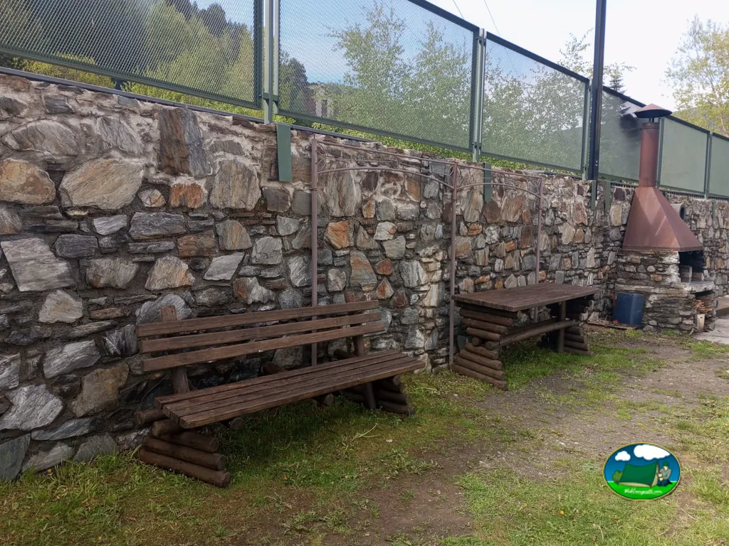 Zona de barbacoas con bancos junto al muro de piedra del Camping Casal