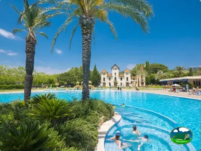 Piscina con vistas a edificio histórico y palmeras del Camping Mas San José, Santa Cristina de Aro (Girona)