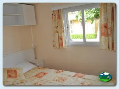 Mobil-home interior con cama y ventana del Camping Mas Patoxas, Pals (Girona)
