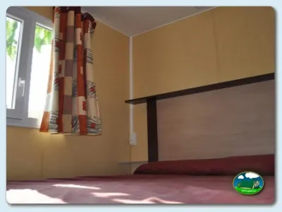 Mobil-home interior con cama y ventana del Camping Mas Patoxas, Pals (Girona)