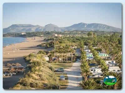 Playa junto al mar con parcelas, palmeras y montaña al fondo del Camping Las Dunas, Sant Pere Pescador (Girona)