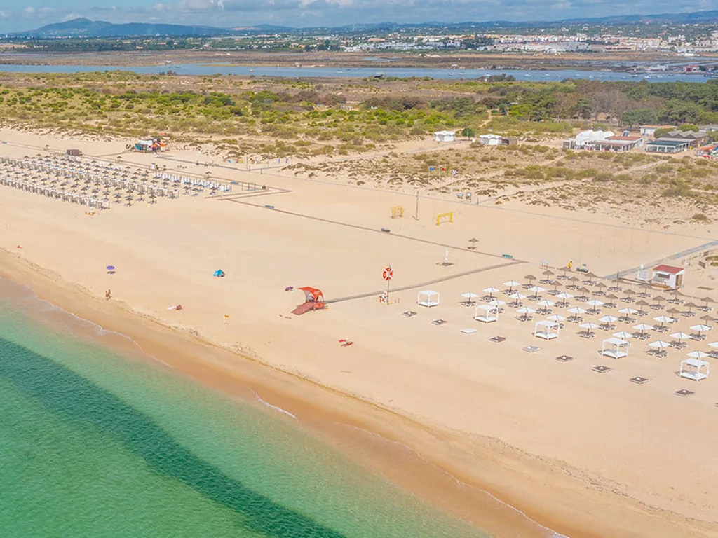 Playa primera línea de mar con sombrillas y zona de baño del Camping ORLA Ilha de Tavira Ecoglamping, Tavira (Faro)