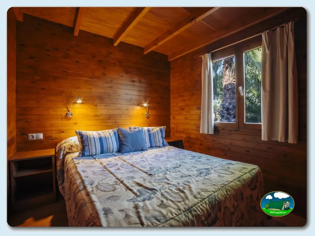 Cabaña con dormitorio de madera y vistas a palmeras del Camping Alannia Costa Blanca, Crevillente (Alicante)