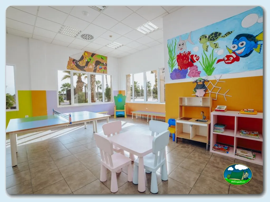 Parque infantil interior colorido con mesas, sillas y zona de juegos del Camping Alannia Costa Blanca, Crevillente (Alicante)
