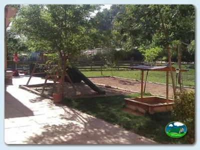 Parque infantil con tobogán y arenero entre árboles del Camping Besalú, Besalú (Girona)