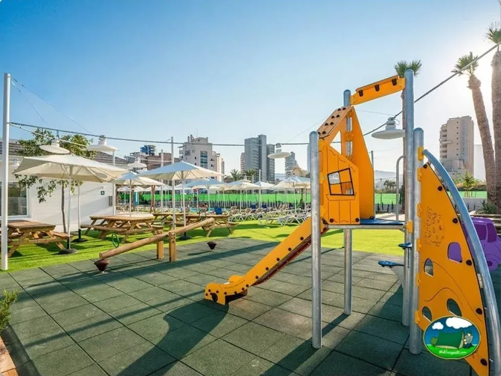 Parque infantil con tobogán y zona de piscina al fondo del Camping Sol de Calpe Austral, Calpe (Alicante)