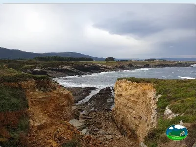 Playa junto al mar con acantilados y vistas a la montaña del Camping Rinlo, Rinlo (Lugo)