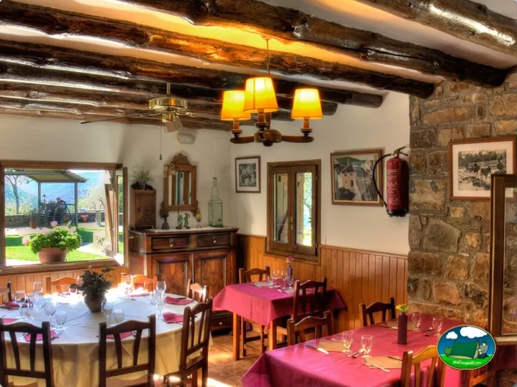 Restaurante interior con vigas de madera y vistas al jardín del Camping Borda Bisaltico, Hecho (Huesca)