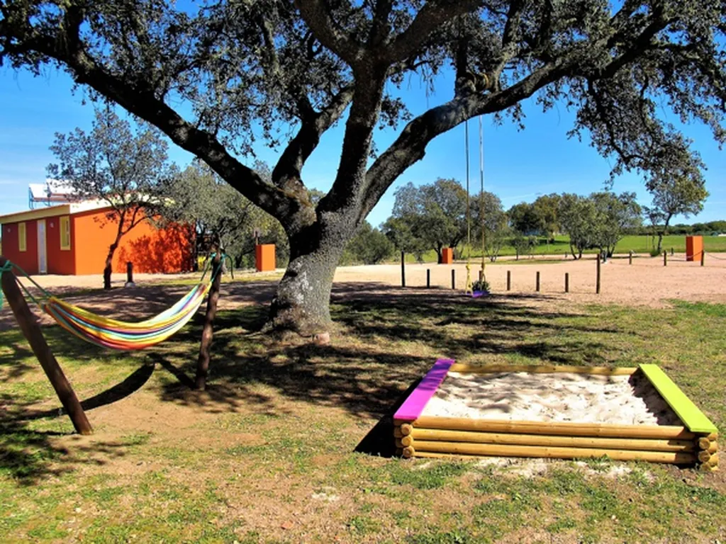 Parque infantil con hamaca y arenero bajo árbol centenario del Camping Puro Alentejo, Elvas (Portalegre)