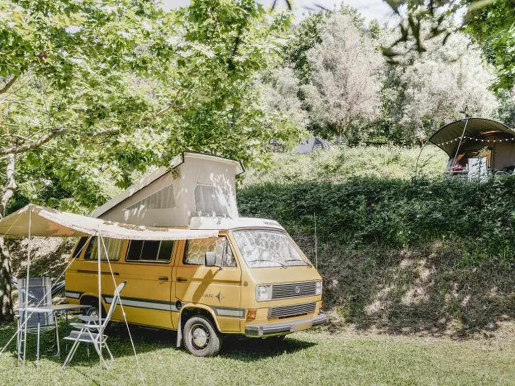 Parcela con autocaravana clásica amarilla y sombrilla del Camping Quinta Valbom, Celorico de Basto (Braga)