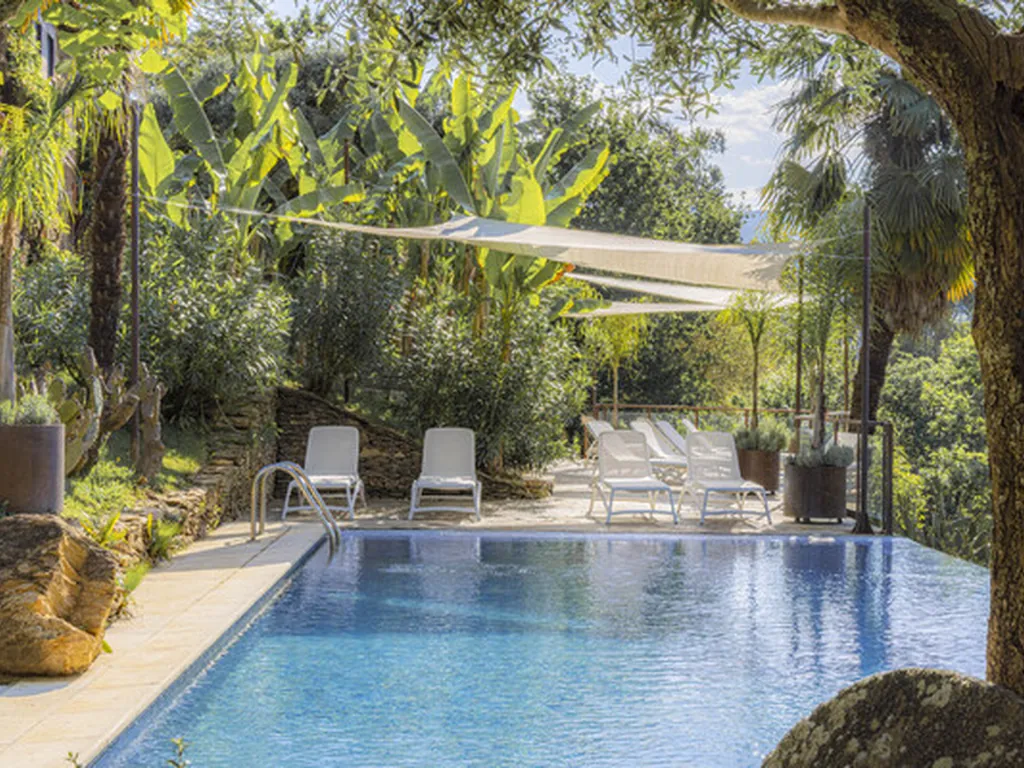 Piscina con tumbonas y sombrilla en jardín del Camping Quinta dos Moinhos, Cabeceiras de Basto (Braga)