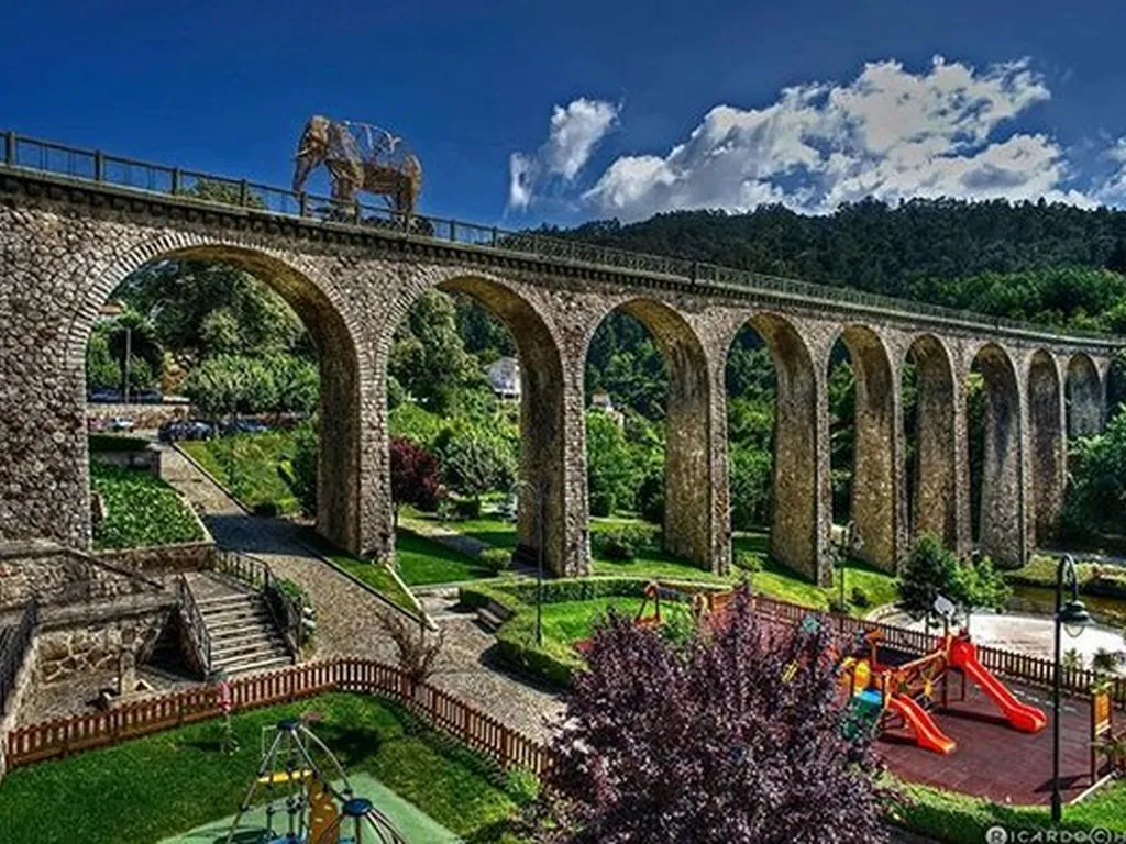 Parque infantil junto al río con viaducto de piedra del Camping Parque de Campismo e Caravanismo de Vouzela, Vouzela (Viseu)