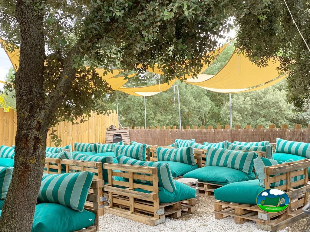 Zona de descanso con sofás palet, sombrillas amarillas y sombra de árboles del Camping Glamping La Bellota, Encinas de Esgueva (Valladolid)