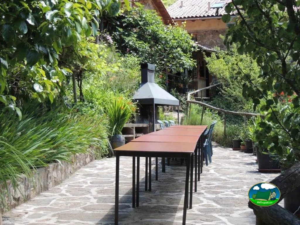 Restaurante con terraza ajardinada y sombrilla del Camping Mas la Bauma, Vallfogona de Ripollès (Girona)