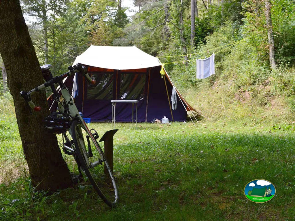 Tienda de acampada en parcela arbolada con bicicleta del Camping Mas la Bauma, Vallfogona de Ripollès (Girona)