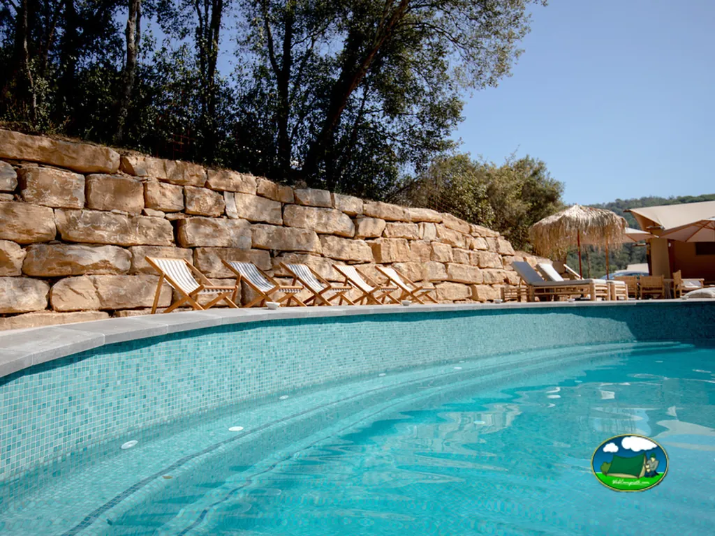 Piscina con tumbonas y muro de piedra del Camping Can Bora Lodges, Sant Gregori (Girona)