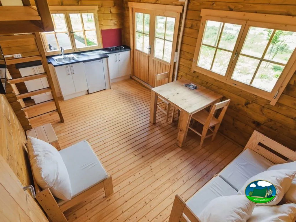 Cabaña de madera interior con cocina, mesa de comedor y camas del Camping Municipal de Artieda, Artieda (Zaragoza)