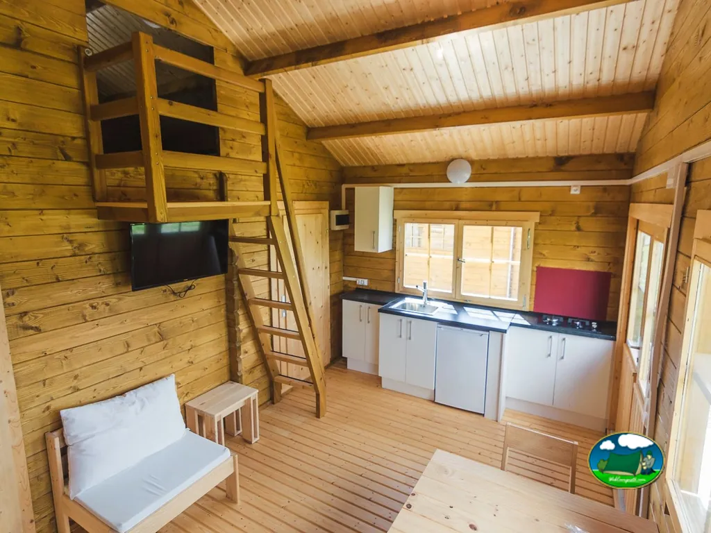 Glamping interior con cama alta, cocina y TV del Camping Municipal de Artieda, Artieda (Zaragoza)