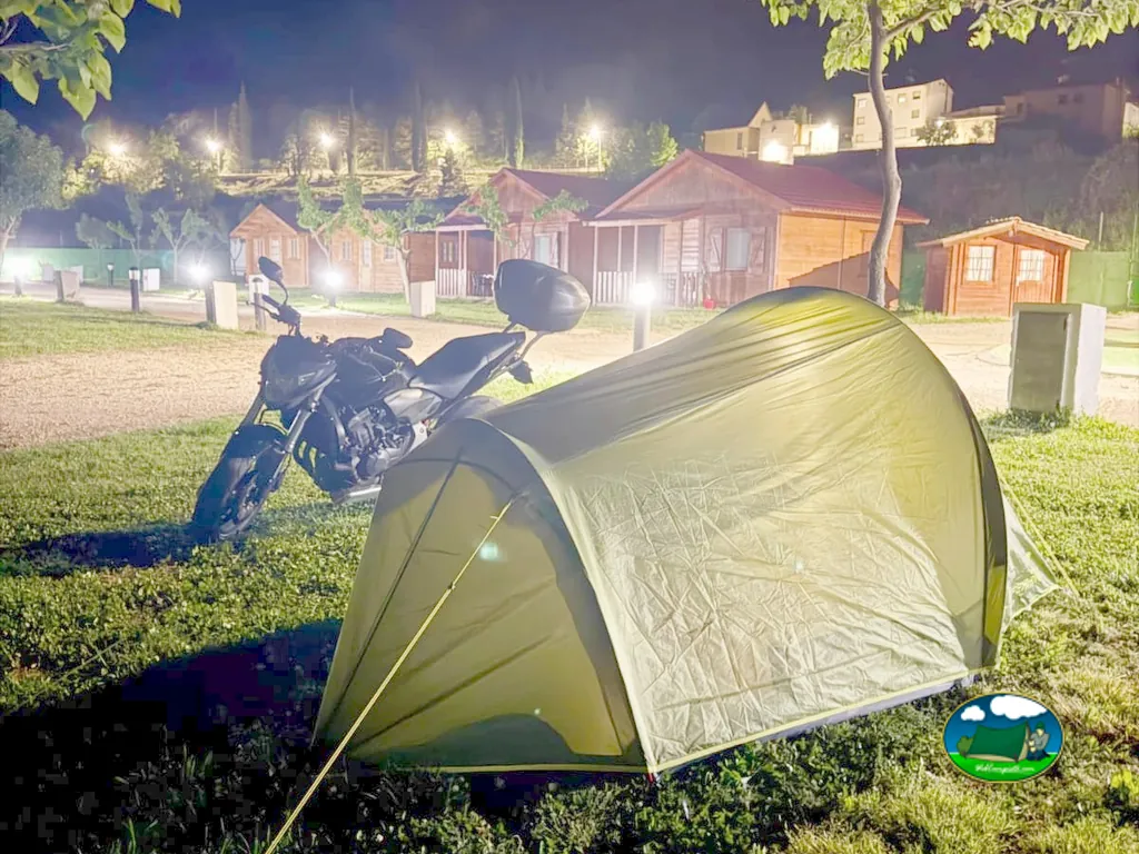 Tienda de acampada en parcela nocturna con bungalow de fondo del Camping Las Aguas, Cañizar del Olivar (Teruel)