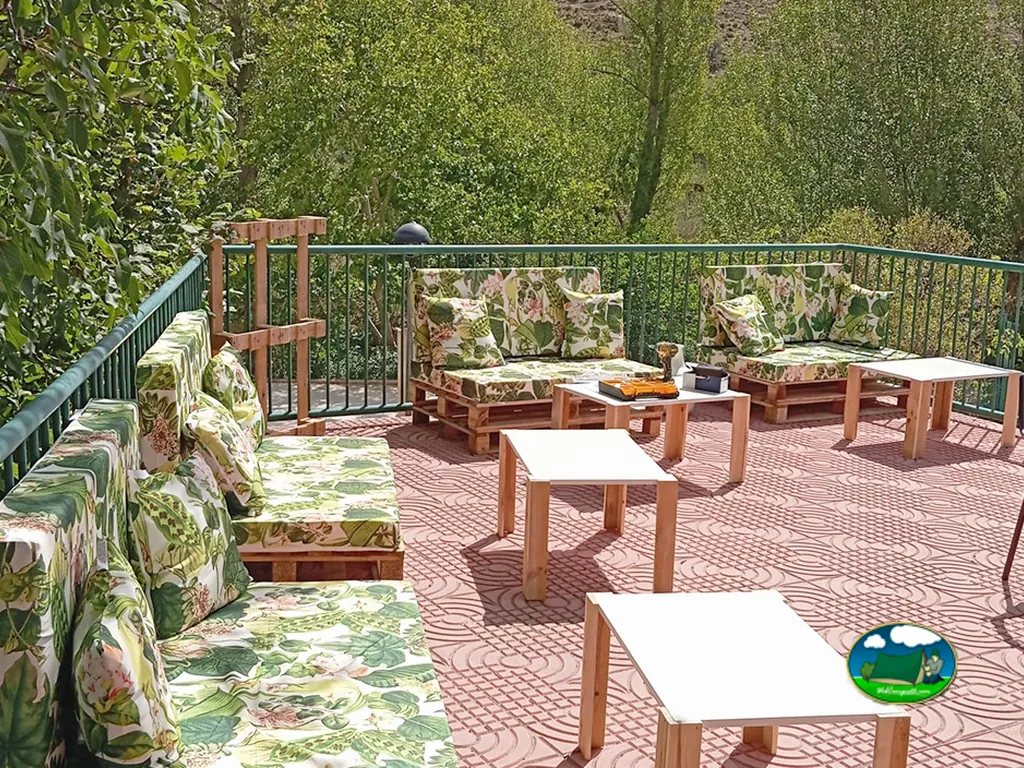 Zona de descanso con sofás y mesas de madera rodeada de vegetación del Camping Las Aguas, Cañizar del Olivar (Teruel)