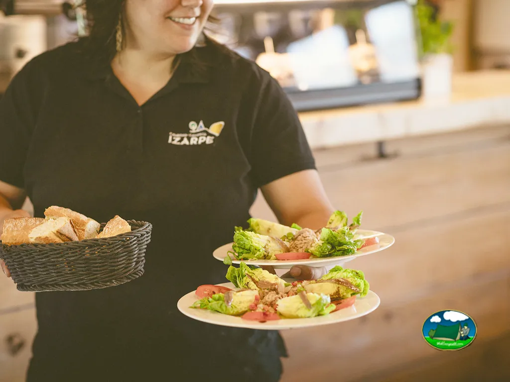 Restaurante, camarera sirviendo ensaladas y pan del Camping Izarpe, Aróstegui (Navarra)