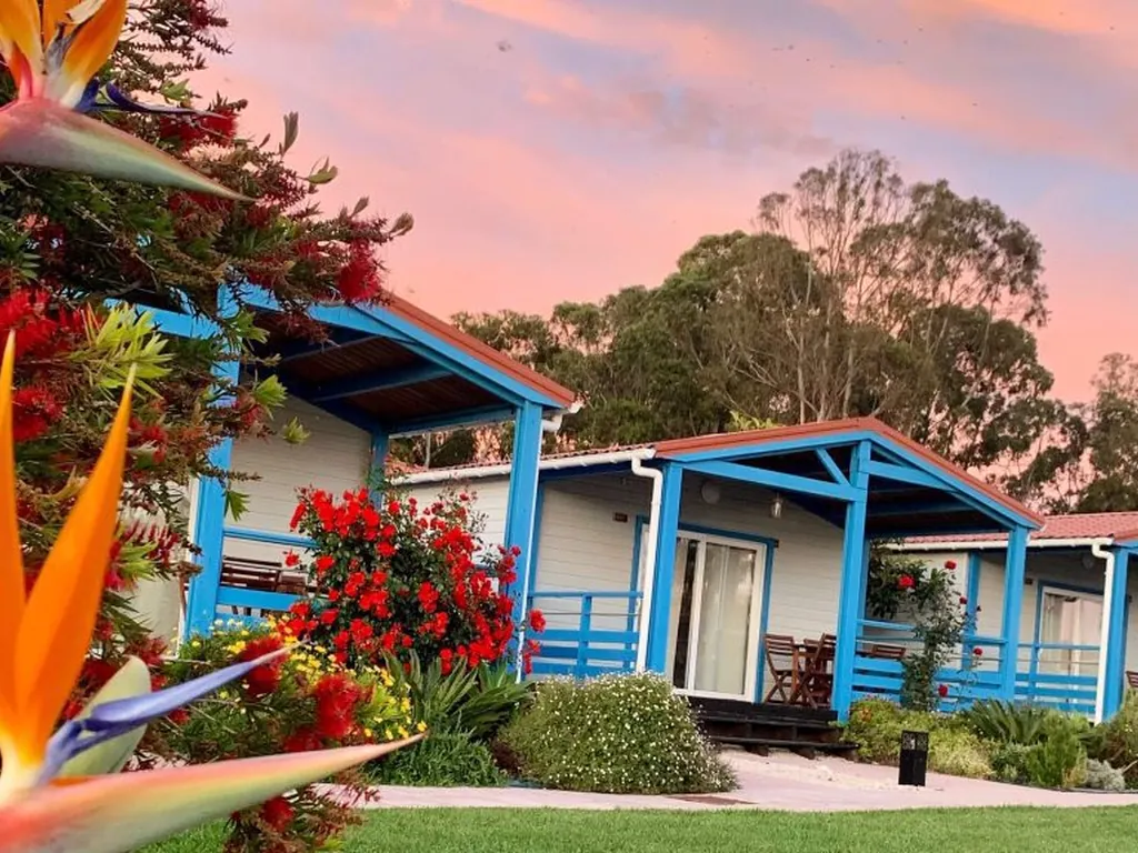 Bungalow con terraza cubierta y flores tropicales al atardecer del Camping Costa do Vizir Beach Village, Porto Covo (Setúbal)