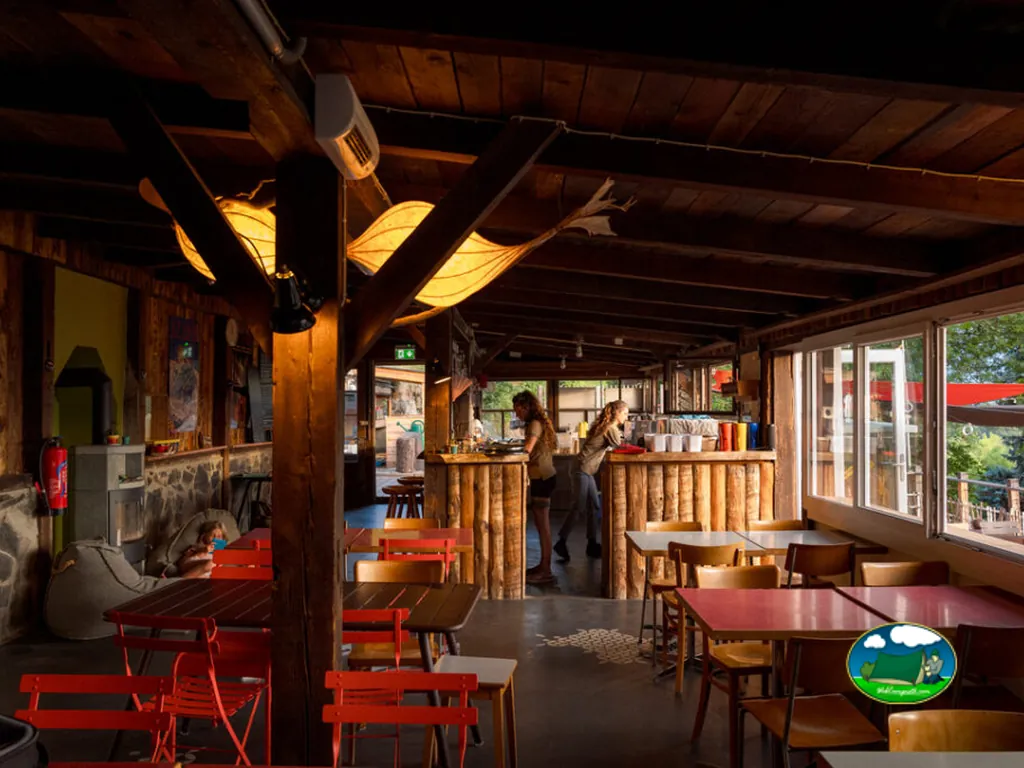 Restaurante bar con barra de madera y mesas del Camping Alp Safari Glamping & Camping, Nax (Valais)