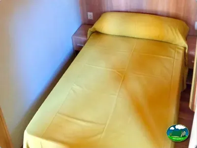 Cama con ropa de cama amarilla en bungalow del Camping Parque Tropical, Estepona (Málaga)