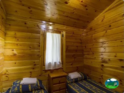 Cabaña interior con dos camas y paredes de madera del Camping Las Lomas, Güejar Sierra (Granada)