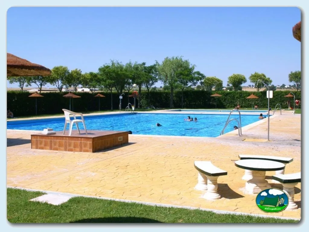Piscina con vistas al campo, sombrillas y zona de arena del Camping Carlos III, La Carlota (Córdoba)