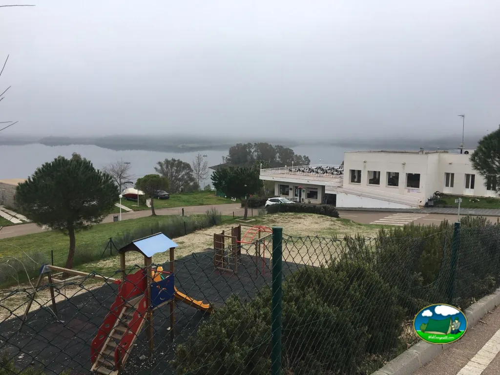 Parque infantil junto al lago con edificio principal del Camping Balcón de Orellana, Orellana la Vieja (Badajoz)