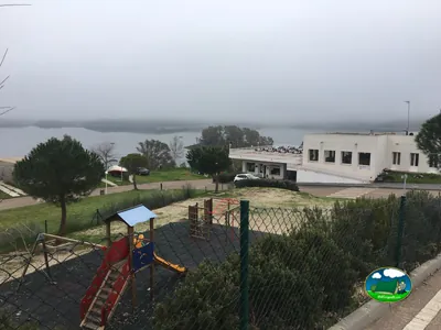 Parque infantil junto al lago con edificio principal del Camping Balcón de Orellana, Orellana la Vieja (Badajoz)