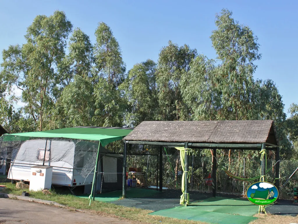 Parcela con toldo y mobil-home entre árboles del Camping Balcón de Orellana, Orellana la Vieja (Badajoz)