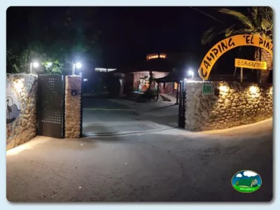 Entrada nocturna con cartel y portón de piedra del Camping El Pinajarro, Hervás (Cáceres)