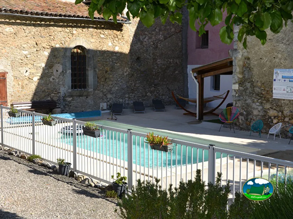 Piscina entre edificios de piedra del Camping La Mare aux Fées, ROQUEFEUIL (Aude)