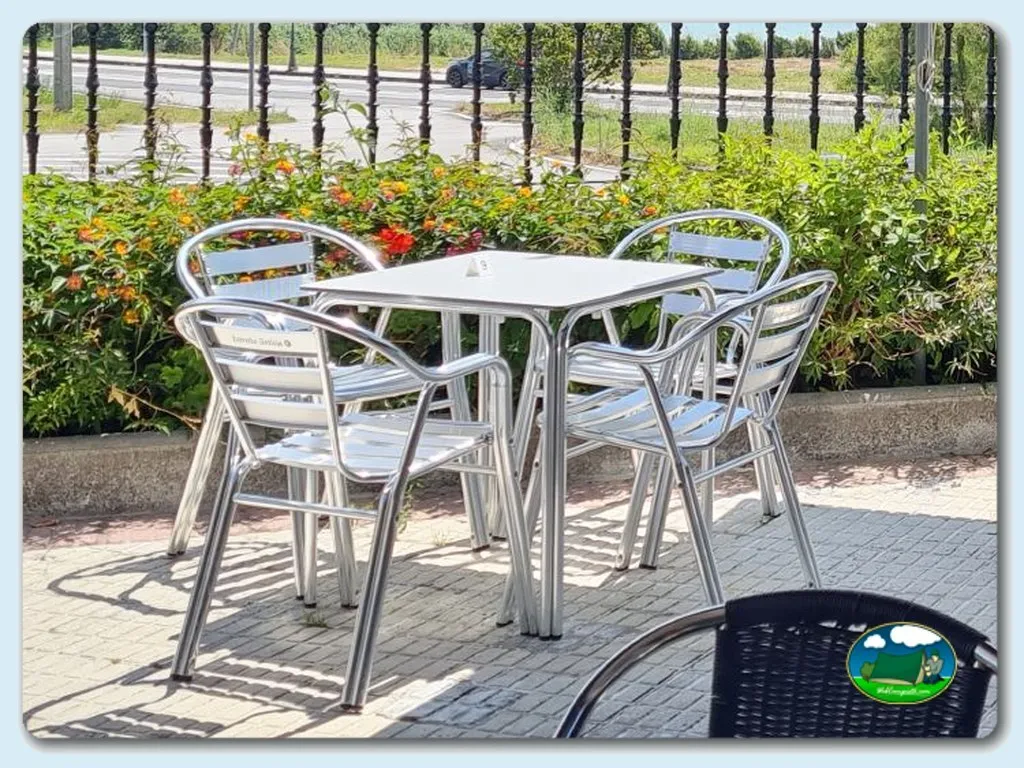 Zona de estar con mesa y sillas de aluminio, flores y valla del Camping Miami Playa, San Vicente do Mar (Pontevedra)